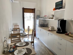 A modern kitchen with a dining area, a TV on the wall, and a view through the door. - BeB Caruso (Sorrento)