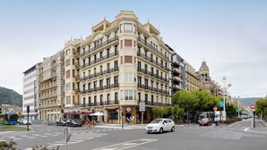 Un edificio de varios pisos con balcones, una calle en su parte frontal y cielo despejado.