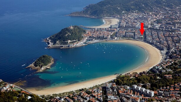 Vista aérea de una ciudad costera con playa, una pequeña isla y una zona urbana densa.