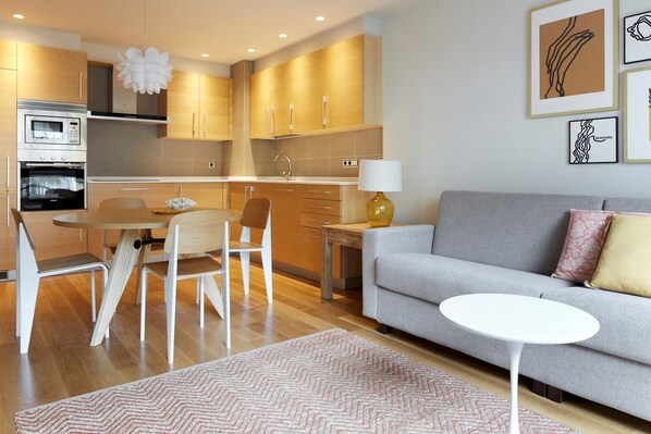 A modern kitchen with wooden cabinets, a dining table with chairs, a sofa, and a small side table. - La Concha Suite 2 by FeelFree Rentals (San Sebastián)