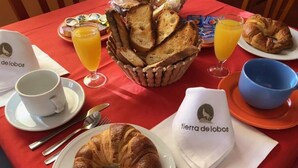 A breakfast setting with croissants, bread, orange juice, and coffee on a red tablecloth. - Hotel Rural Tierra de Lobos (Puebla de Sanabria)