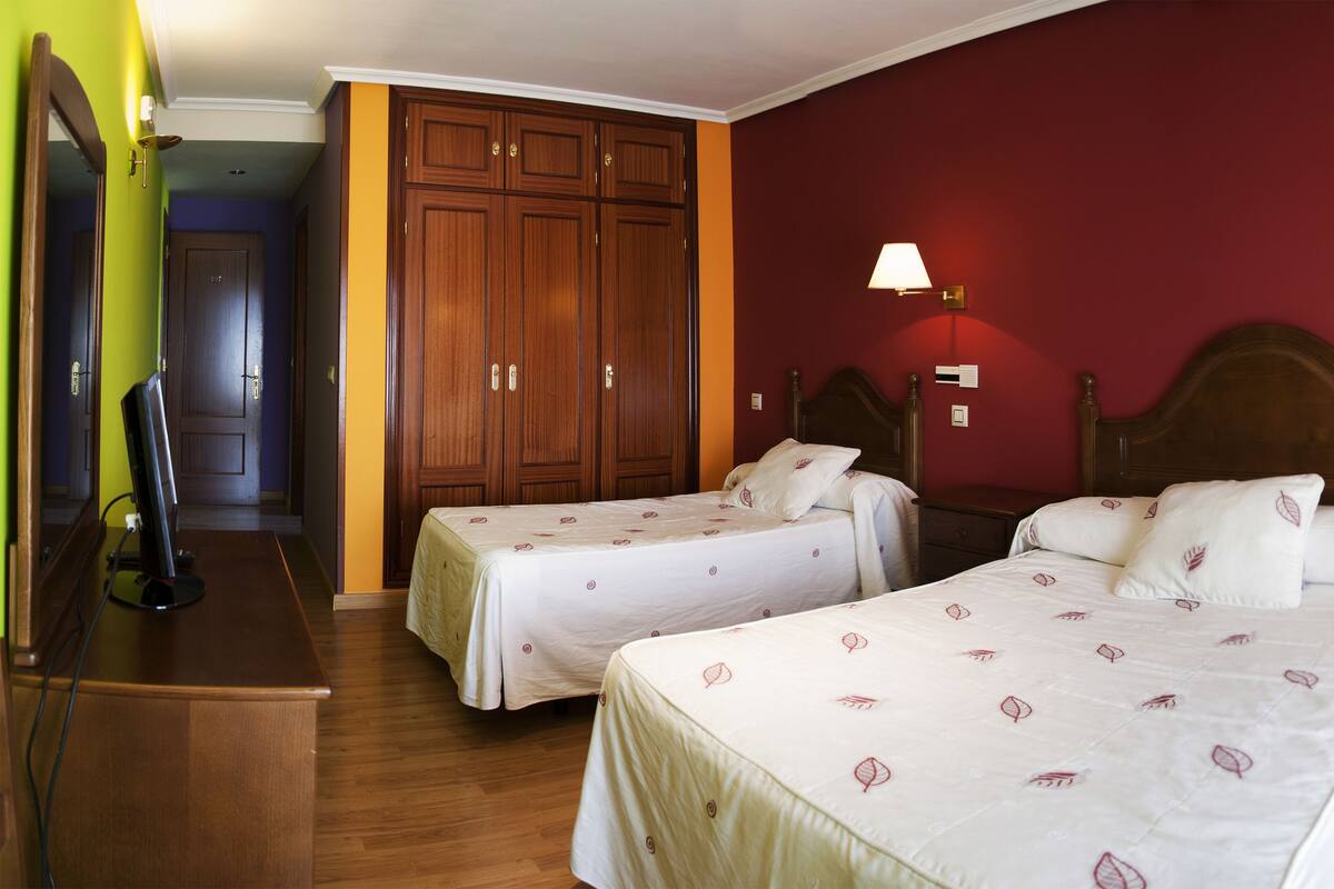 Una habitación de hotel con dos camas, un armario de madera, lámparas de noche y un aparador de madera.
