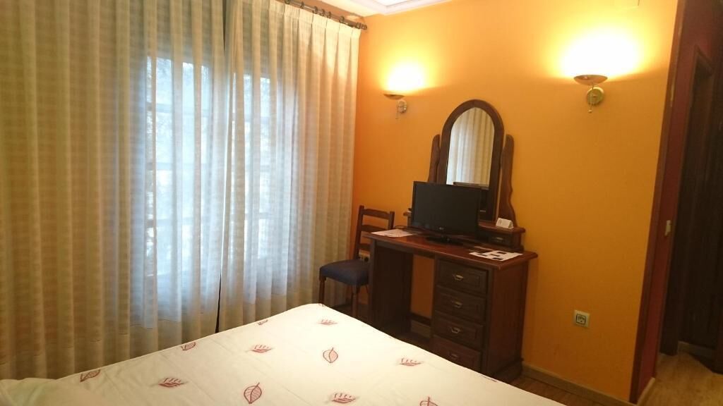 Una habitación de hotel con cama, escritorio con computadora, silla y espejo.