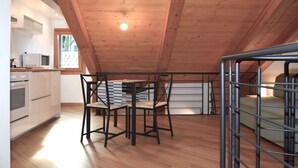 A modern kitchen with wooden beams, a dining area with a table and chairs, and a view of the outdoors through a window.