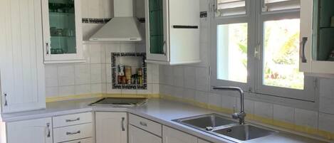Une cuisine moderne avec des meubles blancs, un évier en acier inoxydable et une fenêtre qui laisse entrer la lumière naturelle.