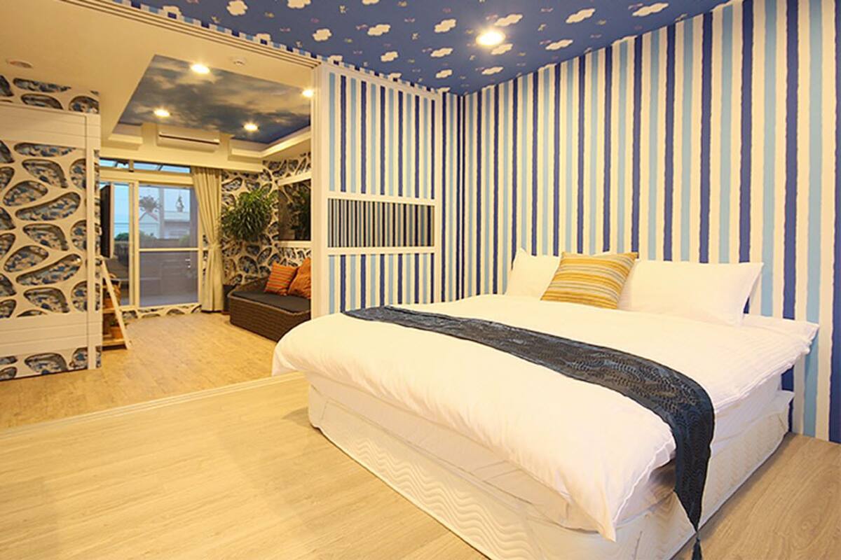 A bedroom with a large bed, striped wallpaper, and a ceiling with cloud patterns.