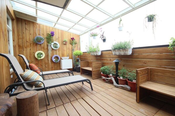 A wooden deck with lounge chairs and benches, surrounded by potted plants and hanging planters.