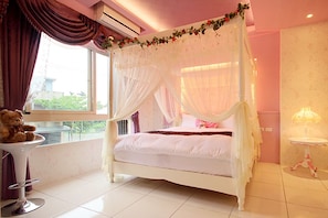 A four-poster bed with a canopy, a bedside table with a lamp, and a teddy bear on a chair.