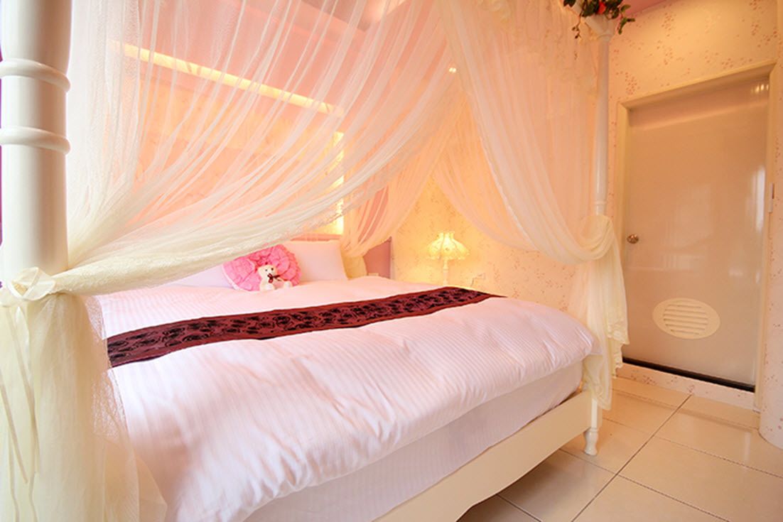 A four-poster bed with a canopy, a bedside table with a lamp, and a white door.