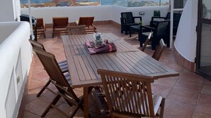 A terrace with a wooden table and chairs, a glass vase, and a view of the sea.