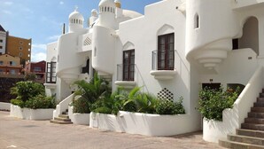 A white building with multiple balconies and a staircase leading to the entrance.