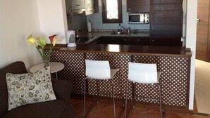 A compact kitchen with a central island, two bar stools, and a small dining table.