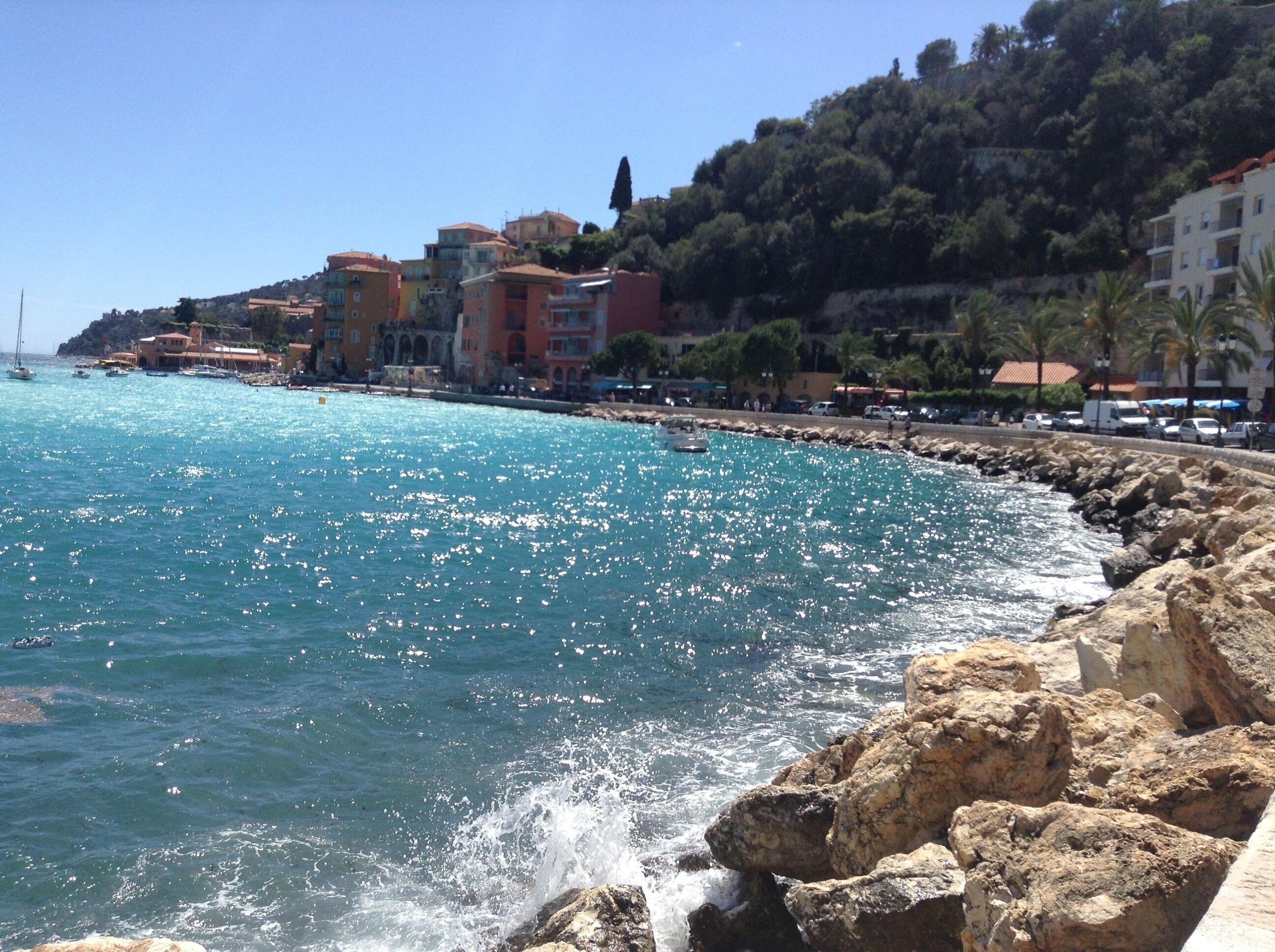 A coastal town with buildings along the shore, rocky coastline, and clear blue sea.