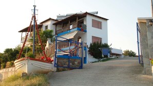 A coastal building with a balcony, a boat docked outside, and a stone wall. - Demi Studios (Aristotelis)