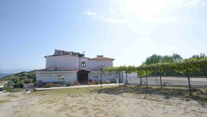 A two-story house with a tiled roof, a covered driveway, and a fenced garden area. - Demi Studios (Aristotelis)