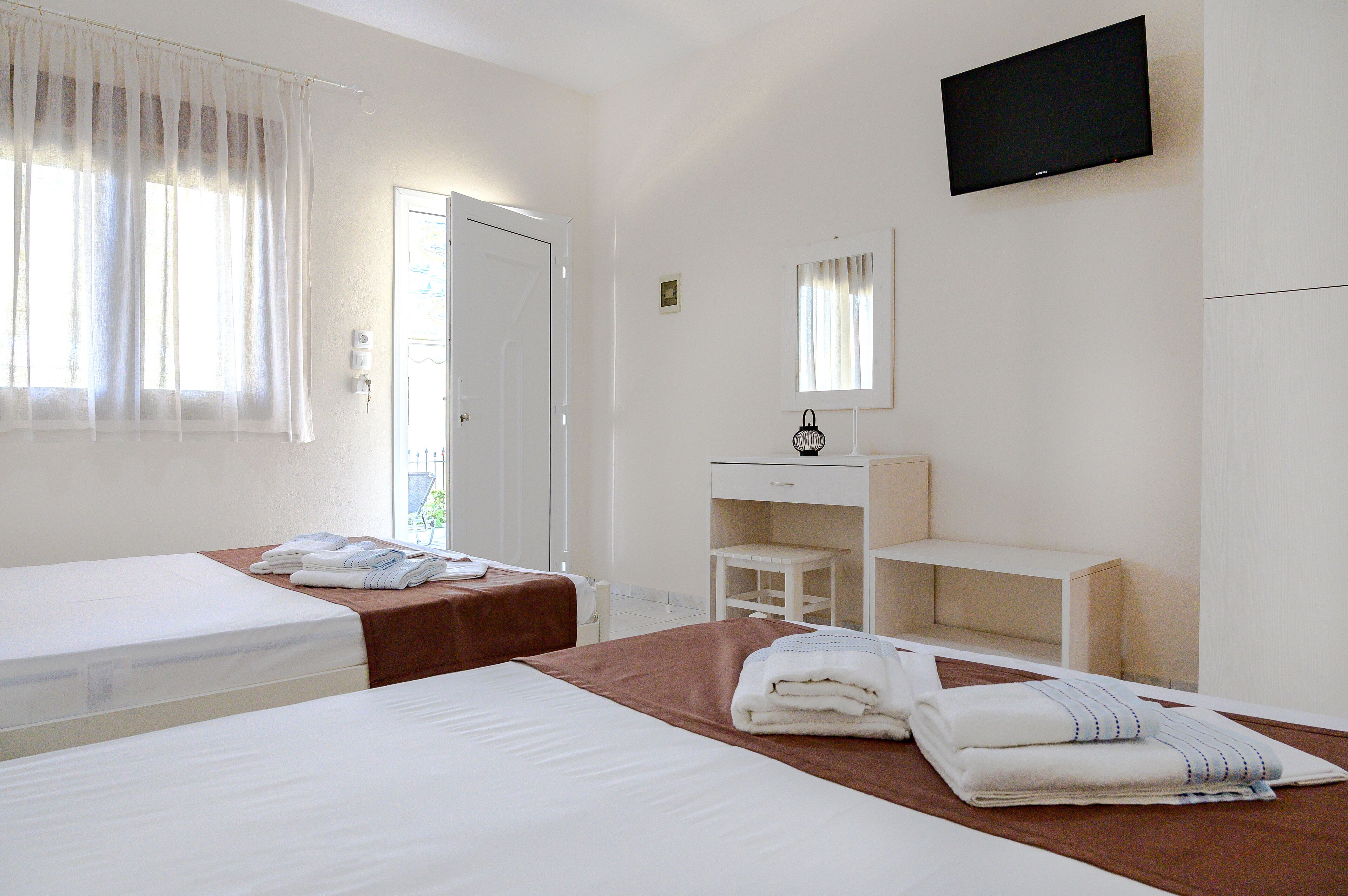 Une chambre d’hôtel avec deux lits, un bureau, une chaise, une télévision et une fenêtre avec des rideaux.