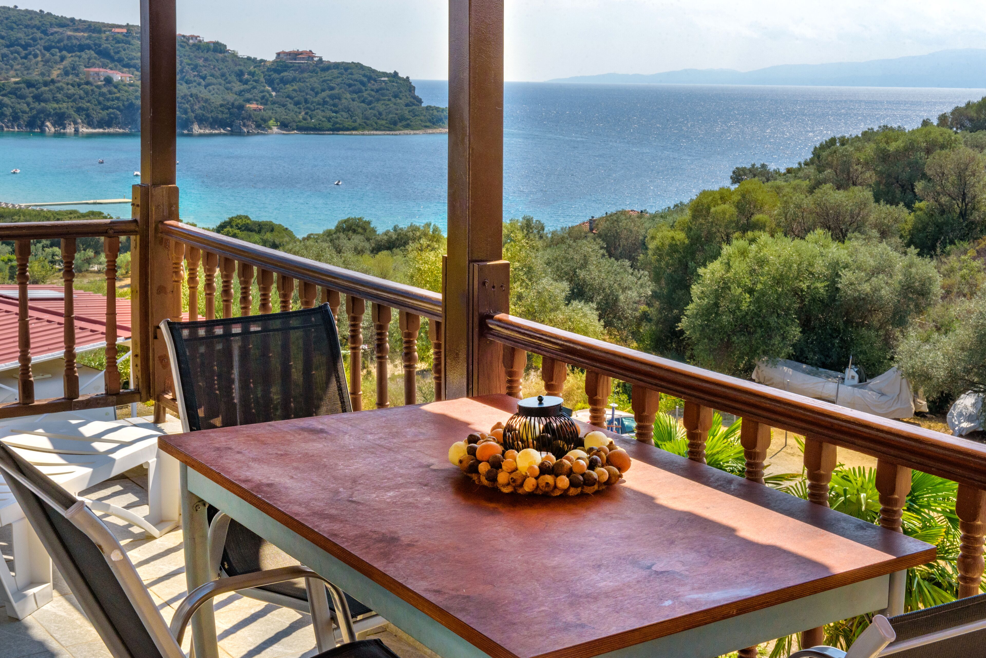Un balcon avec une table et des chaises, donnant sur un paysage côtier avec des arbres et une vue sur la mer.