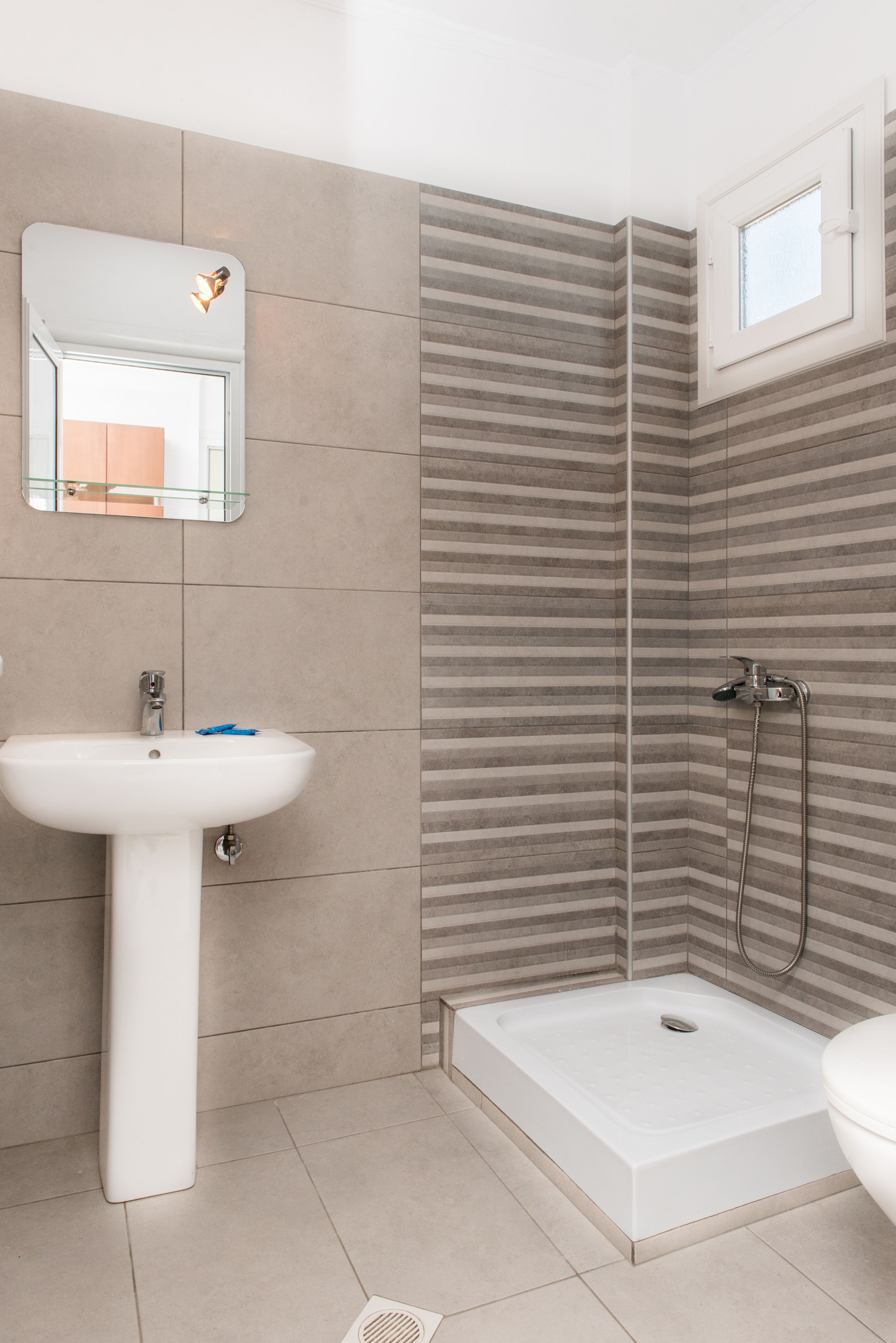 Un baño con un lavamanos blanco, una ducha con puerta de cristal y una pequeña ventana sobre la ducha.