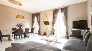 Een moderne woonkamer met een bank, een glazen salontafel, een eethoek met stoelen en een televisie.