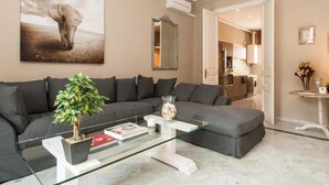 Een moderne woonkamer met een grijze modulaire bank, een glazen salontafel en een potplant.