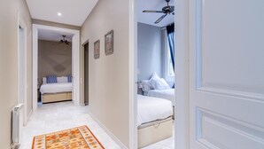 Een gang die leidt naar een slaapkamer met een bed, een plafondventilator en een raam met gordijnen.