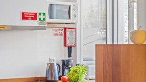 A modern kitchen with a microwave, kettle, and coffee maker. There is a sign indicating an emergency exit and a first aid kit on the wall. - Hillside - By Wehost (Funchal)