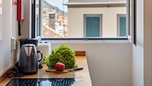 A kitchen counter with a kettle, a toaster, a cutting board with a tomato, and a potted plant. - Hillside - By Wehost (Funchal)