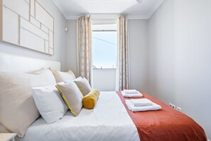 Une chambre d’hôtel avec un lit, des oreillers, une couverture rouge et une fenêtre avec des rideaux.