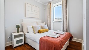 A bedroom with a bed, nightstand, and window with curtains. - Hillside - By Wehost (Funchal)