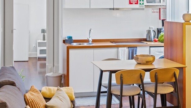 A modern kitchen with white cabinets, a hanging light fixture, and a dining area with a wooden table and chairs. - Hillside - By Wehost (Funchal)