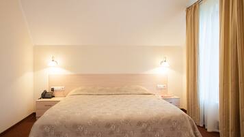 A hotel room with a large bed, two bedside lamps, a telephone, and a window with curtains.