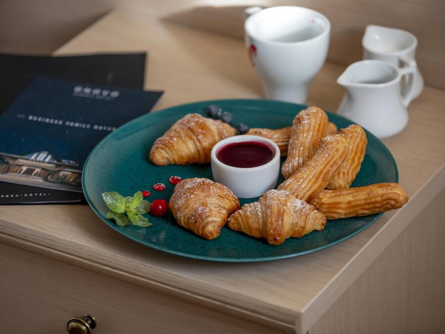 A plate of pastries with a small bowl of jam and two white cups on a wooden table.