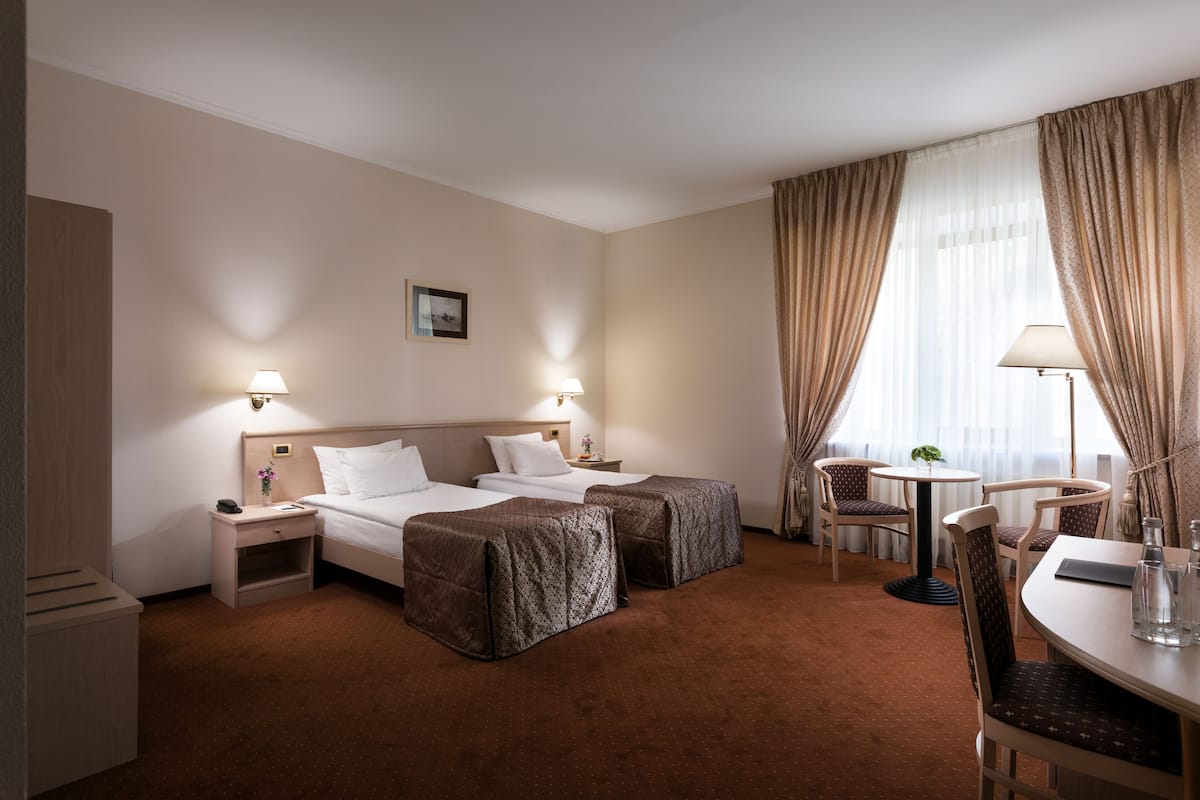 Camera d'albergo con due letti, un piccolo tavolo con sedie, una scrivania e una finestra con tende.