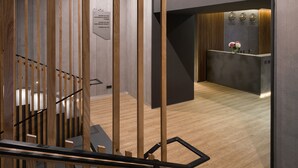 A modern hotel reception area with a wooden reception desk, a sign for 'ONOVO Dendra Hotel', and a staircase with wooden railings. - Onovo (Kyiv)