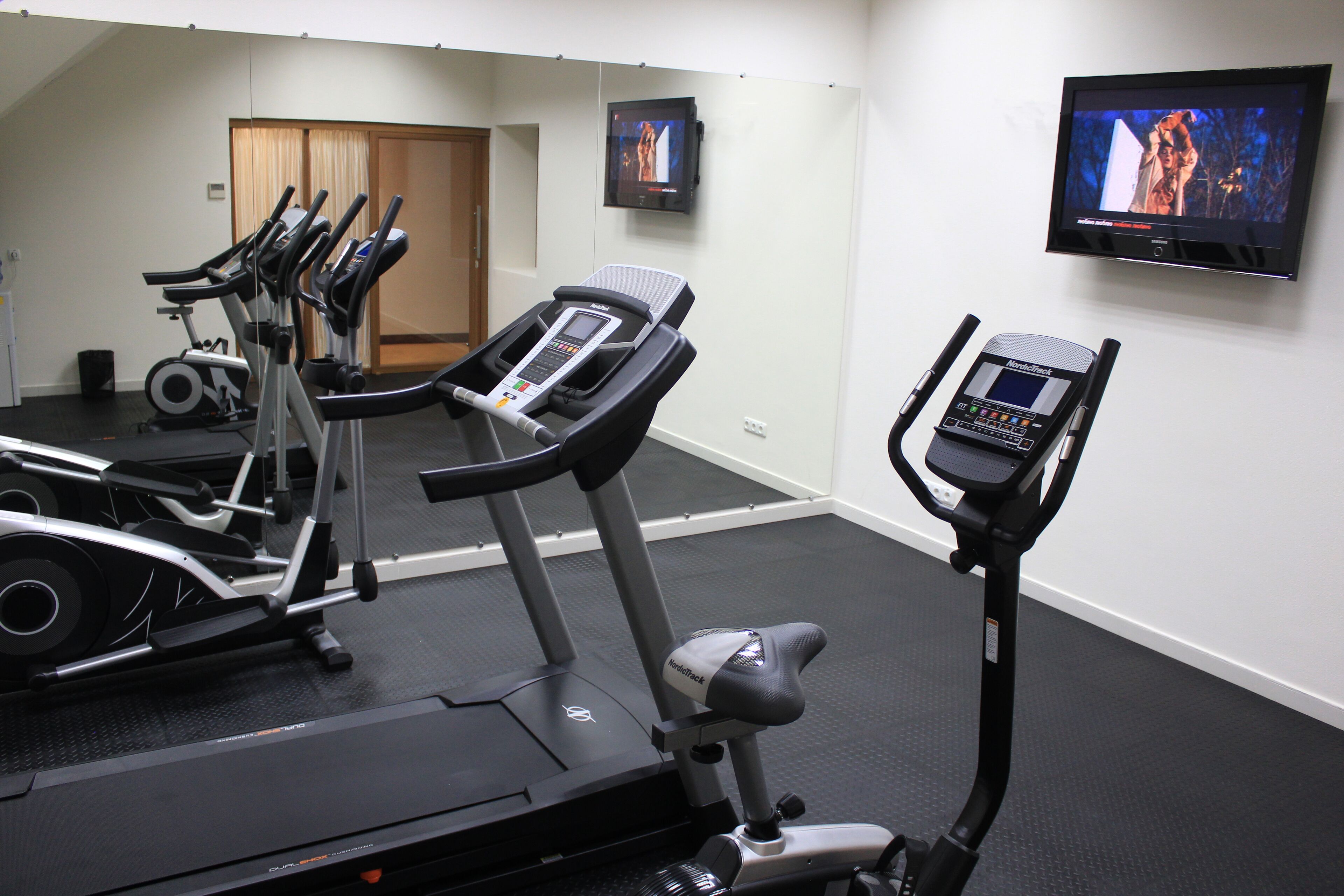 Ein Fitnessraum mit Laufbändern, Ergometer und einem an der Wand befestigten Fernseher.