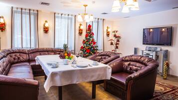 A dining area with a round table set for four, surrounded by leather sofas. A Christmas tree is in the background.
