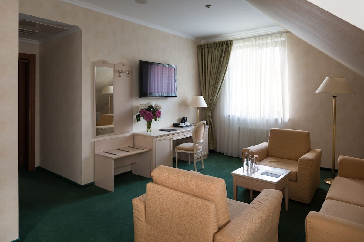 Una camera d'albergo con una scrivania, due poltrone, un divano, una televisione, una lampada e una finestra con tende.
