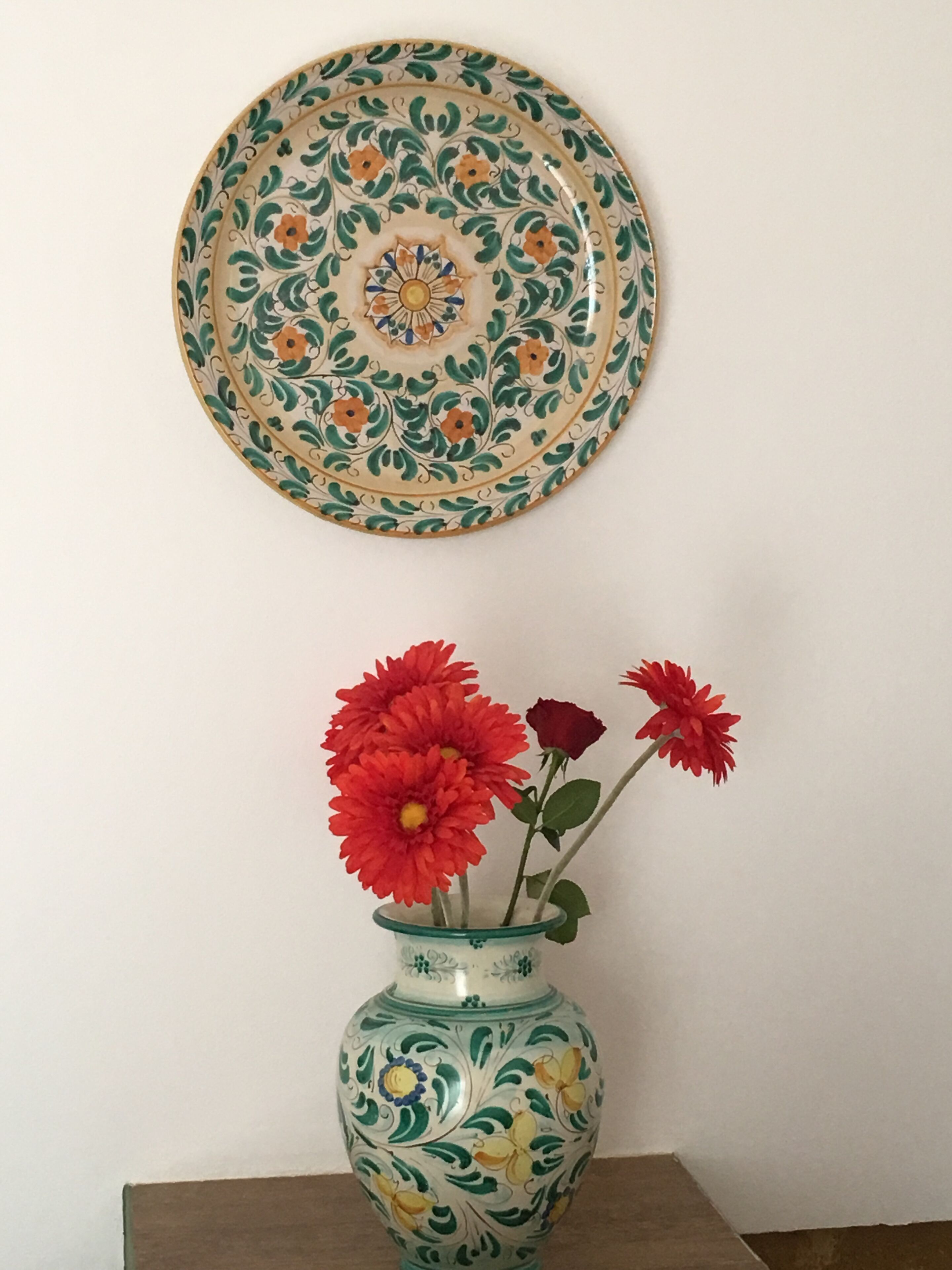 A decorative plate with a floral pattern and a vase with red flowers.