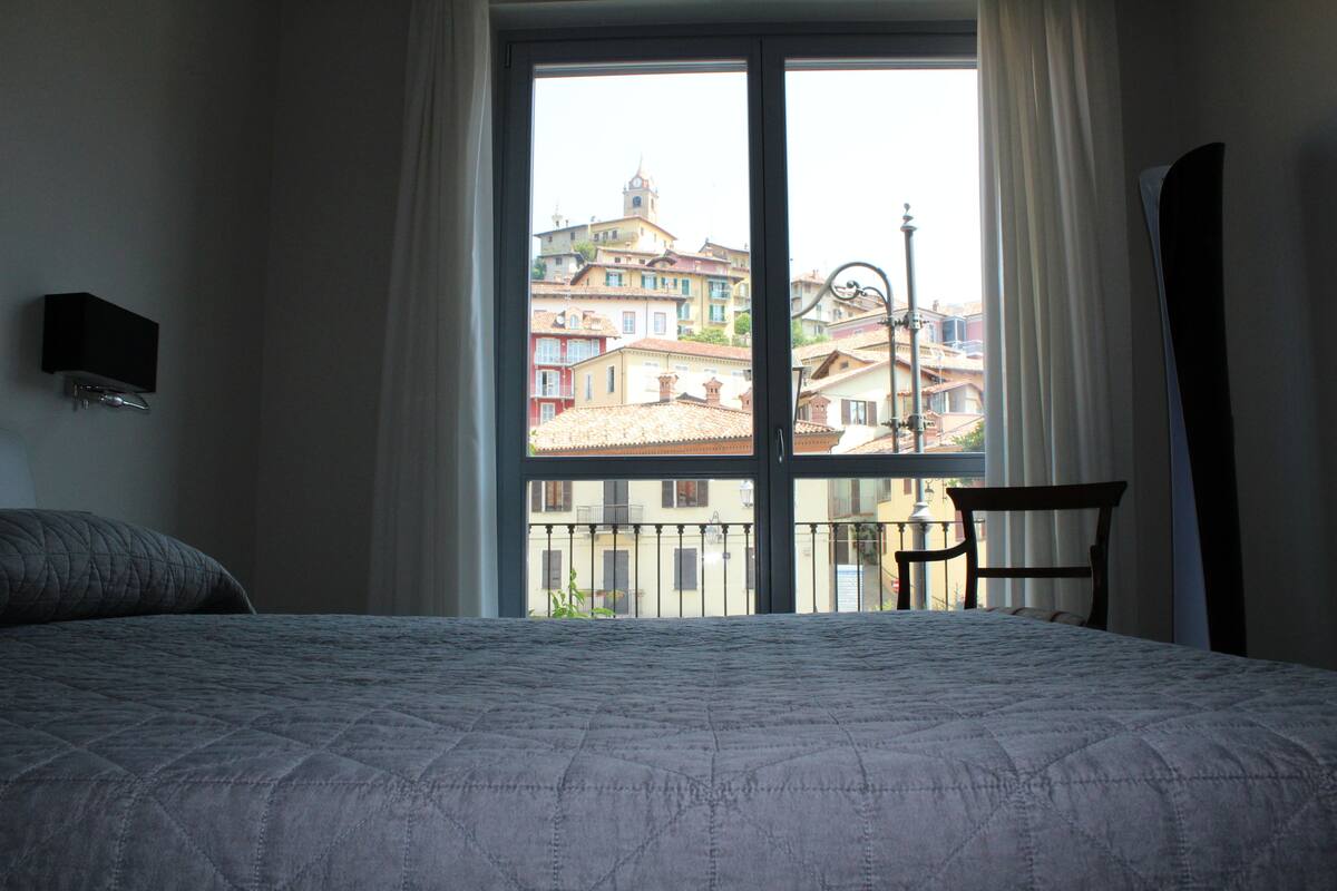 Ein Hotelzimmer mit großem Fenster, einem Bett mit gesteppter Bettdecke, einem Sessel und einem an der Wand befestigten Fernseher.