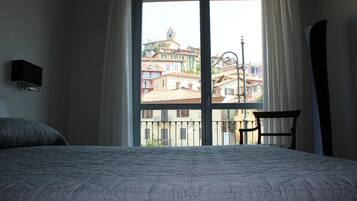 Una habitación de hotel con un ventanal grande, una cama con colcha acolchada, una silla y un televisor de pared.