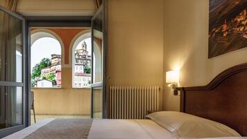 Una habitación de hotel con una cama, vistas a través de una puerta de cristal, un radiador y una lámpara fijada a la pared.