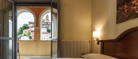 A hotel room with a bed, a view through a glass door, a radiator, and a wall-mounted light fixture.