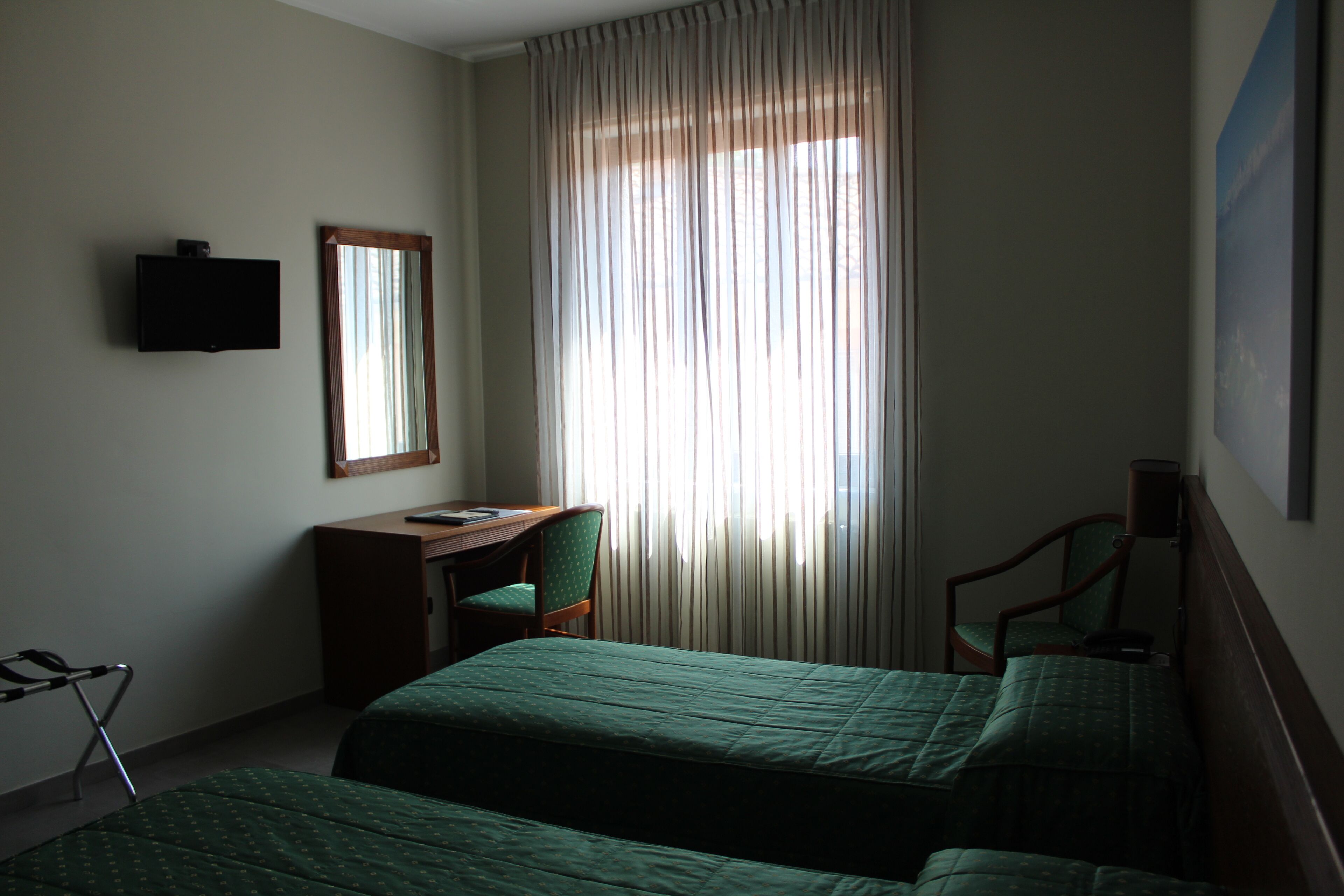 A hotel room with two beds, a desk, a chair, a television, and a window with curtains.