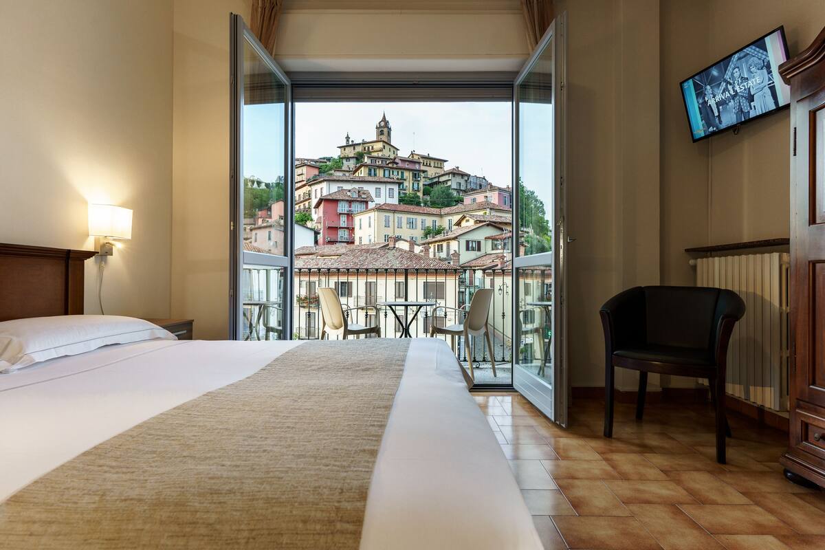 Ein Hotelzimmer mit einem großen Bett, einem Sessel, einem Fernseher und einem Balkon mit Blick auf die Stadt.