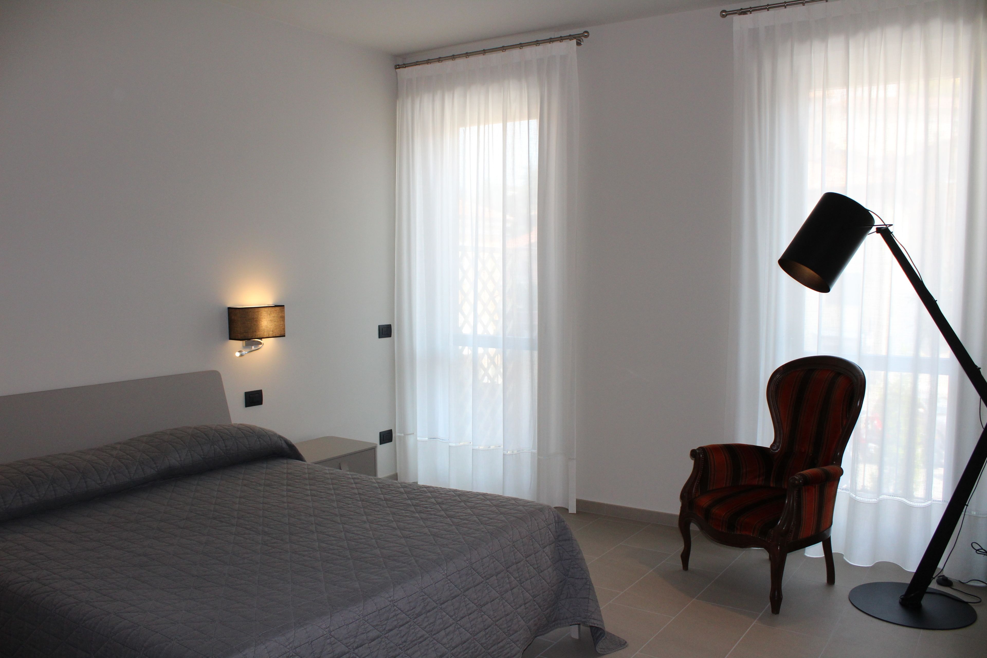 A hotel room with a bed, a chair, a desk, and a floor lamp.