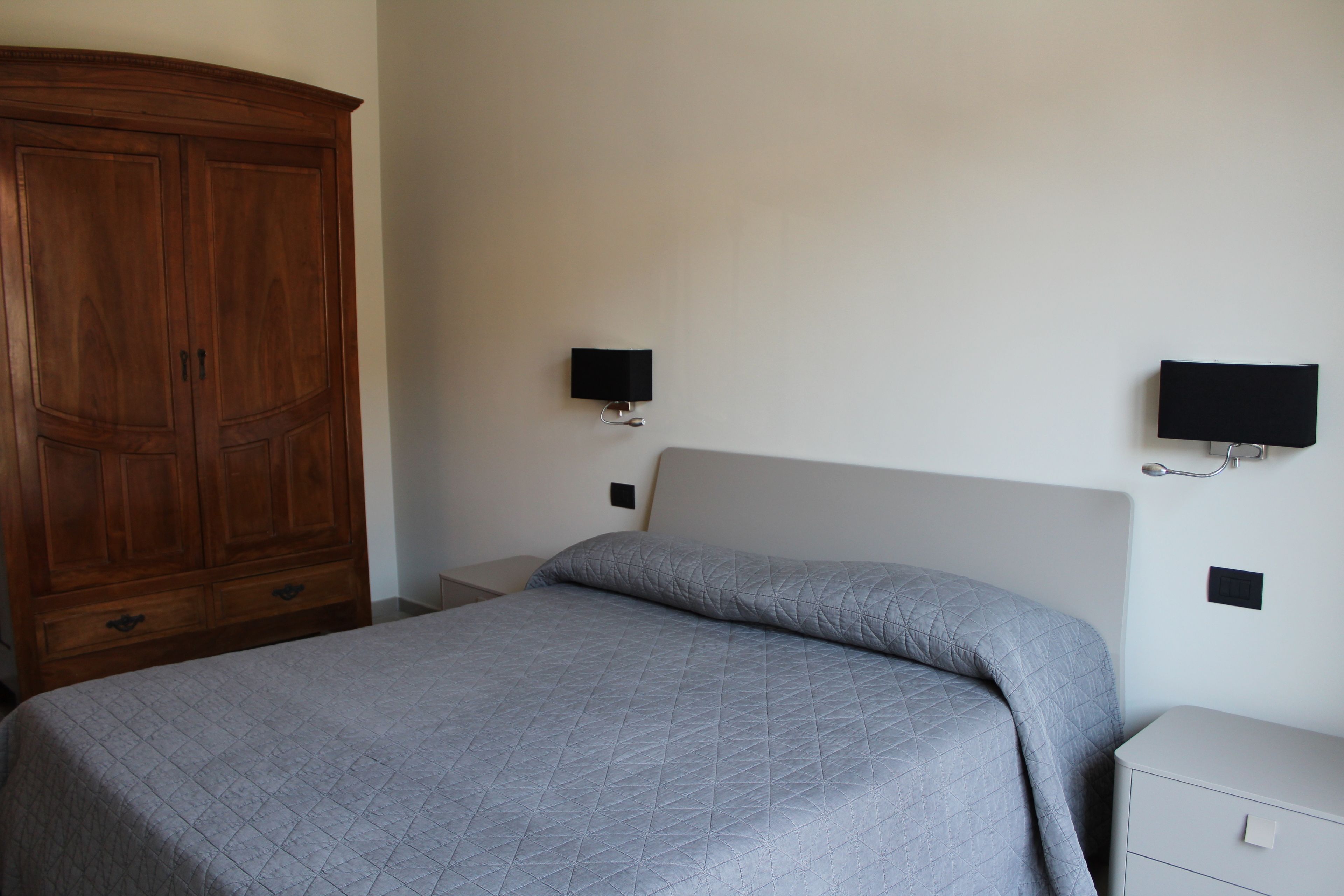 A bedroom with a bed, a wooden wardrobe, a bedside table, and a wall-mounted TV.