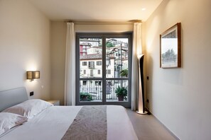 A bedroom with a bed, a nightstand, a floor lamp, a window with curtains, and a framed picture on the wall. - Hotel Il Grappolo d'Oro (Monforte d'Alba)