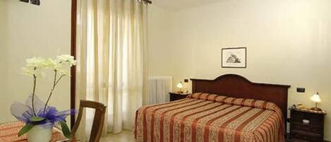 A hotel room with a bed, a chair, a table with a vase of flowers, a nightstand, and a picture on the wall.