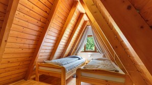 Een kleine slaapkamer op zolder met twee houten stapelbedden, een raam met uitzicht op groen en een houten plafond.