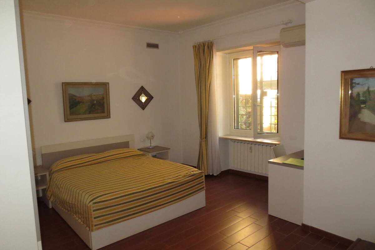 Une chambre à coucher comprenant un lit, une table de chevet, une fenêtre avec des rideaux, un radiateur et un tableau accroché au mur.
